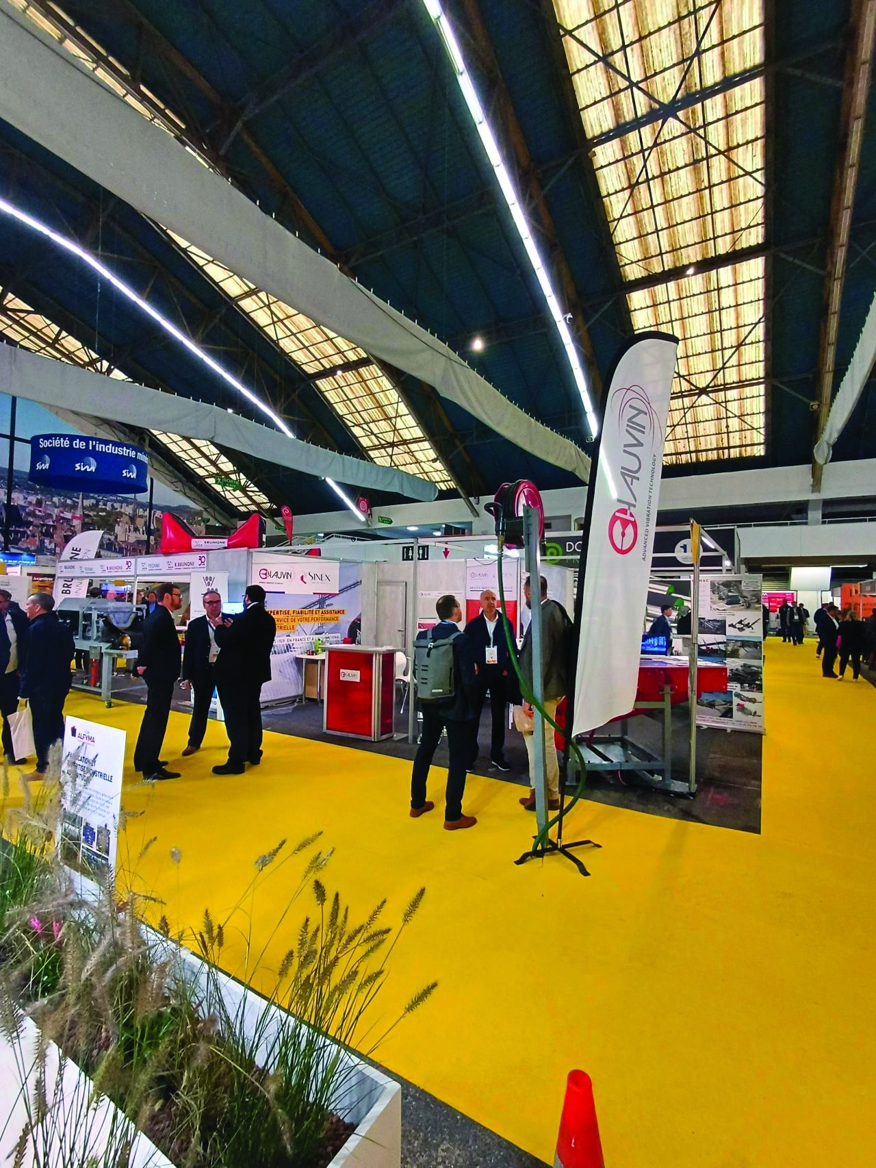 Vue d’un salon industriel avec des stands d’exposition, des représentants d’entreprises en discussion et un tapis jaune caractéristique. L’événement se déroule sous une grande structure avec un éclairage moderne.